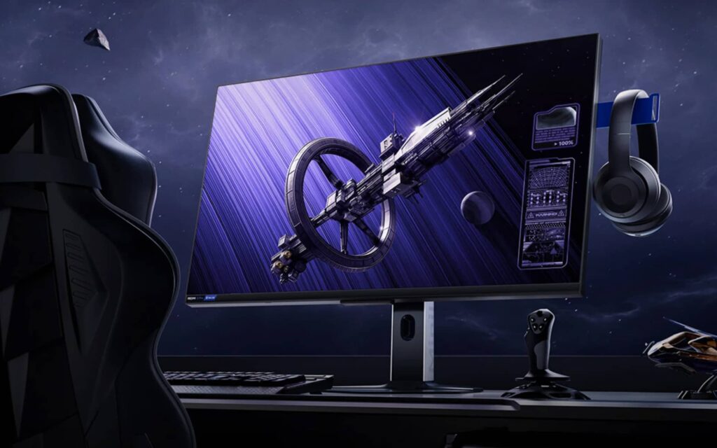 Wide monitor displays futuristic sci‑fi spaceship artwork; gaming chair, keyboard, and headset shown in a space setting