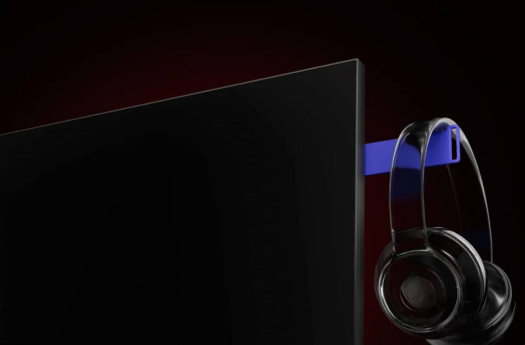 Close-up of a sleek flat-screen monitor with a blue headset draped over its edge against a dark red background.