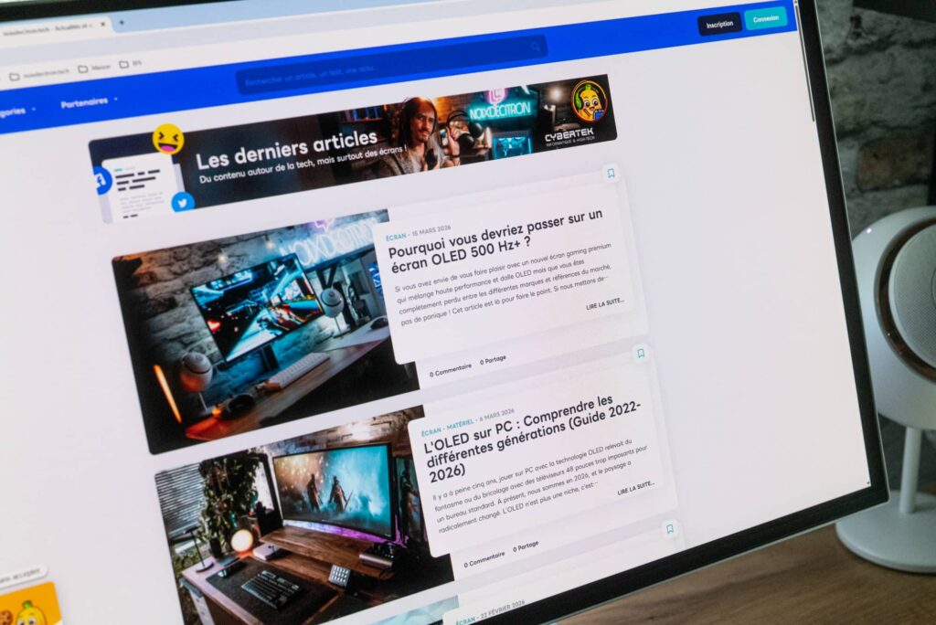 A computer monitor showing a tech blog with article cards about OLED and gaming setups on a blue header page banner.