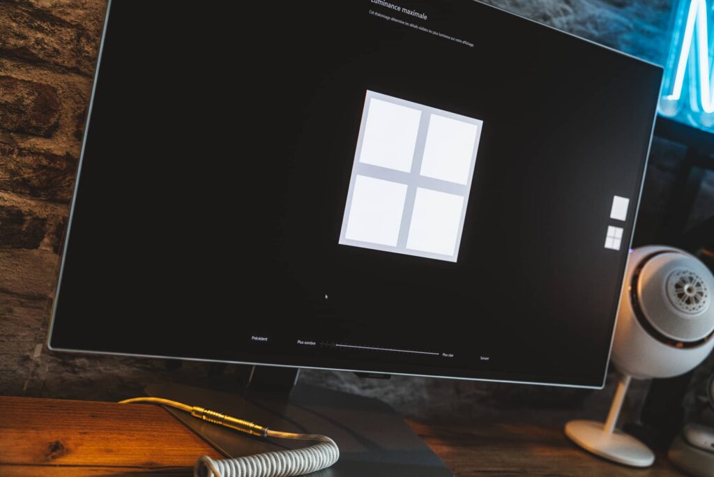 Monitor on a wooden desk shows the Windows logo on a black screen, with a coiled cable in the foreground.