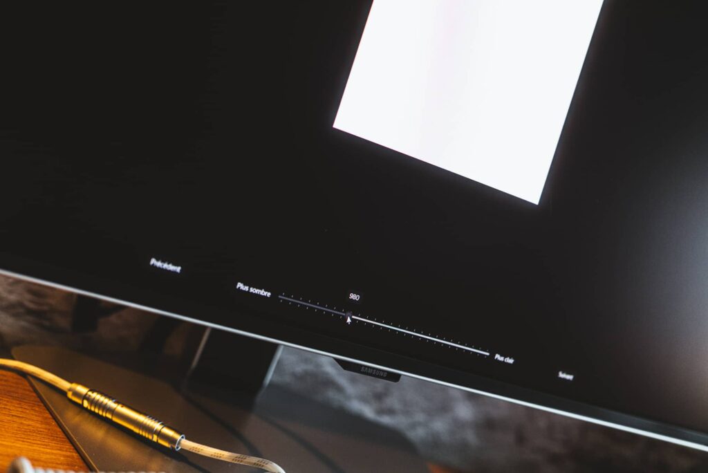 Samsung monitor with a brightness slider visible on screen and a bright white shape, cables in the foreground.
