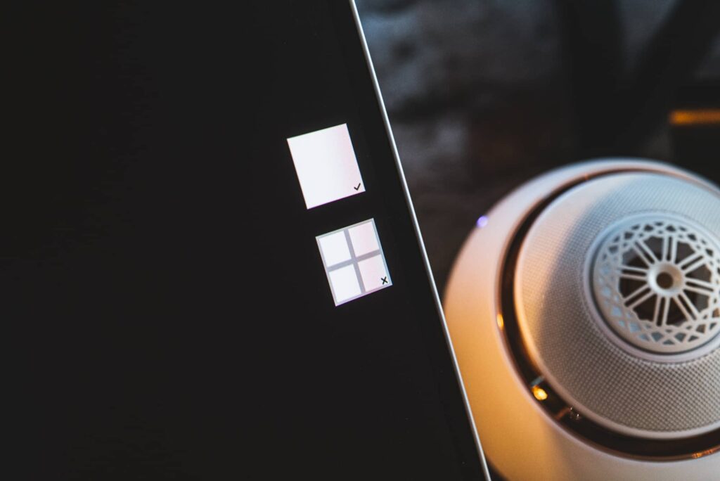 Close-up of a device edge with two square app icons; a silver over-ear headphone sits to the right.