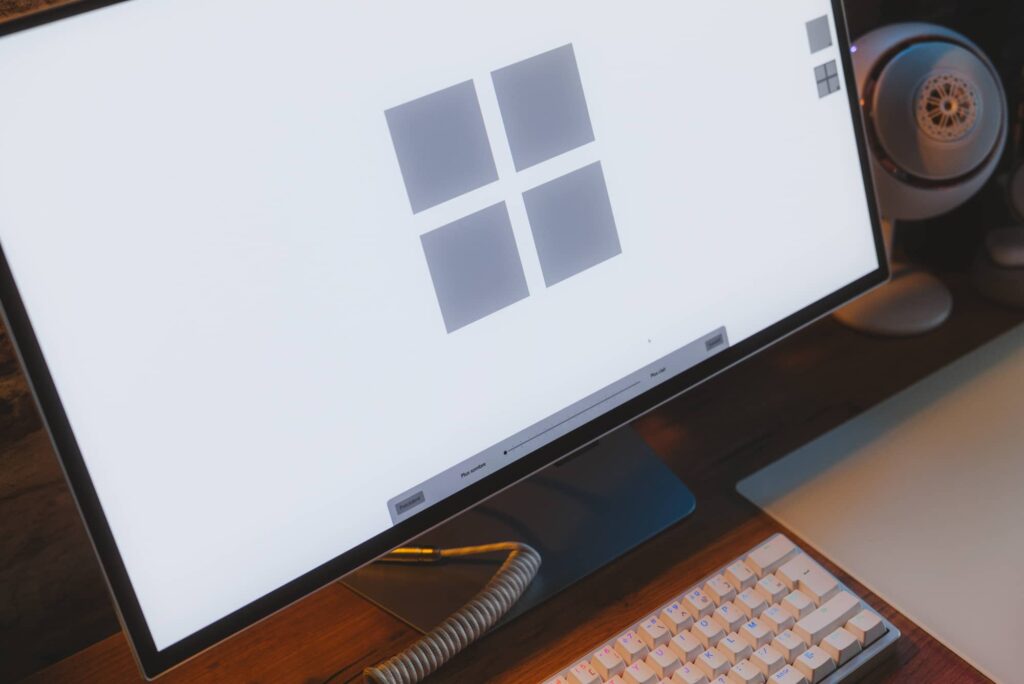 Monitor displays a large Windows logo on a white screen, with a keyboard and desk items in view.