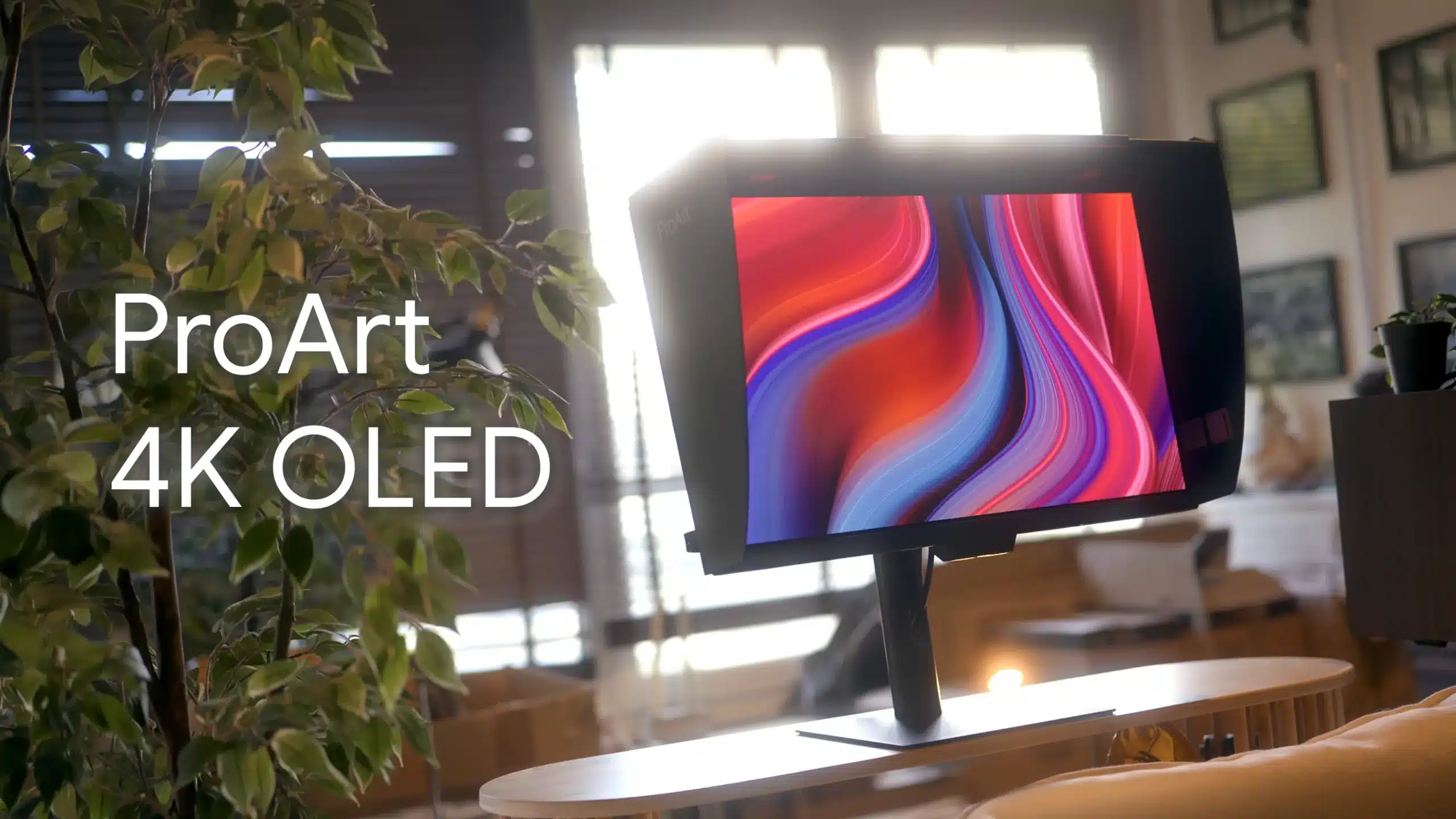 ProArt 4K OLED monitor on a stand in a bright showroom, with a leafy plant in the foreground.